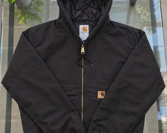 May include: A black hooded jacket with a full-length front zipper, ribbed cuffs, and a ribbed hem. The jacket features a Carhartt brand label on the chest and a matching label on the inside collar. The interior is lined with black quilted fabric.