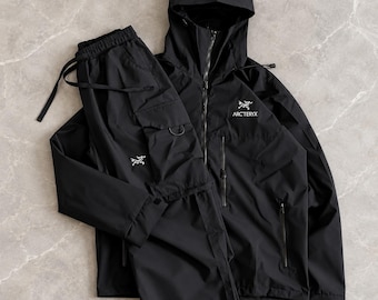 Pode incluir: Um conjunto preto de casaco com capuz e calças cargo. O casaco apresenta um fecho frontal, um capuz e o logótipo branco Arc'teryx no peito. As calças incluem bolsos cargo laterais com um pequeno logótipo branco Arc'teryx na coxa.