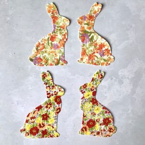 May include: Four fabric bunny shapes with a floral pattern in shades of yellow, orange, and red. The bunnies are cut out and ready to be used for crafting projects.