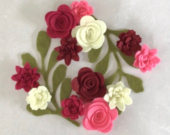 Può includere: Una ghirlanda di fiori in feltro con fiori color borgogna, rosa e bianchi. La ghirlanda è fatta di foglie e fiori in feltro.