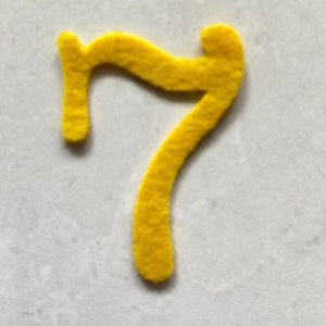K&ouml;nnte beinhalten: Eine gelbe Filz-Zahl Sieben. Die Zahl ist ausgeschnitten und hat eine flauschige Textur.