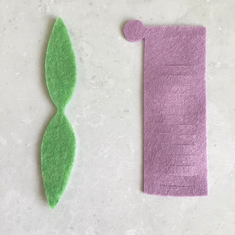 May include: Two felt pieces for crafting. One is a green leaf shape and the other is a purple rectangle with a circle at the top.