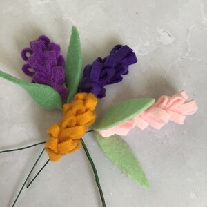May include: A bouquet of felt flowers with green leaves and wire stems. The flowers are purple, pink, and orange.