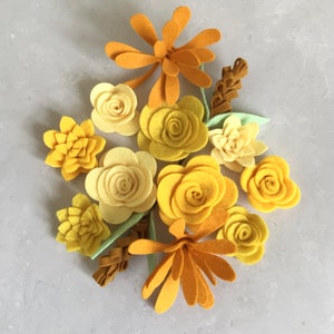May include: A collection of felt flowers in shades of yellow and orange. The flowers are arranged in a bouquet and include various shapes and sizes.
