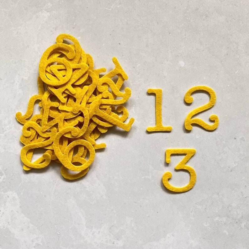 K&ouml;nnte beinhalten: Ein Stapel gelber Filzbuchstaben, darunter die Zahlen 1, 2 und 3.