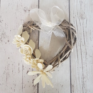 May include: A heart-shaped wicker wreath decorated with off-white felt flowers and a sheer white ribbon.