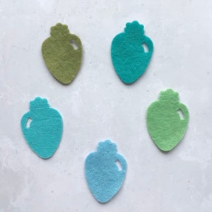 Puede incluir: Cinco adornos de fieltro con forma de bombilla en varios tonos de verde y azul.