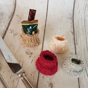 May include: Four small knitted bags with beaded trim. The bags are in beige, red, and gray. One bag is filled with a small chocolate bar wrapped in green foil.