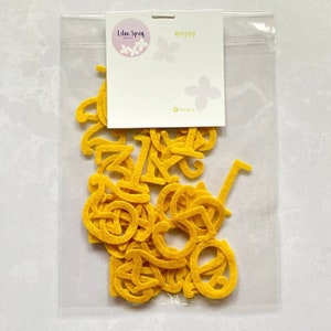 K&ouml;nnte beinhalten: Eine transparente Plastikt&uuml;te gef&uuml;llt mit gelben Filzbuchstaben, Zahlen von 0 bis 9. Die T&uuml;te hat ein wei&szlig;es Etikett mit dem Text "Lilac Sprig Designs" und "enjoy" darauf gedruckt.