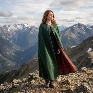Può includere: Un mantello lungo fino ai piedi in lana verde bosco con una fodera a quadri scozzesi rossi e verdi. Il capo è fissato al collo con una spilla circolare in metallo argentato e si indossa sopra una maglia nera a maniche lunghe e pantaloni scuri.