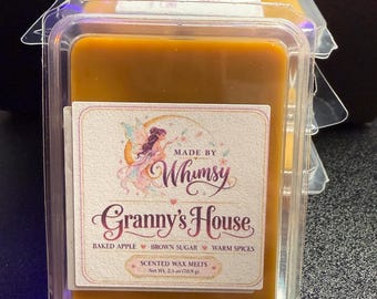 May include: A rectangular package of golden-brown scented wax melts in a clear plastic container. The label features a fairy illustration and the text: Made by Whimsy, Granny's House, Baked Apple, Brown Sugar, Warm Spices, Scented Wax Melts, Net Wt. 2.5 oz (70.9 g).