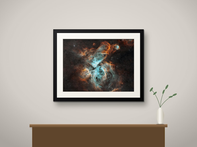 May include: A framed wall art print featuring a deep space nebula with vibrant swirls of bright cyan and burnt orange gas clouds set against a dark, star-filled background, enclosed in a simple black frame with a white mat border.