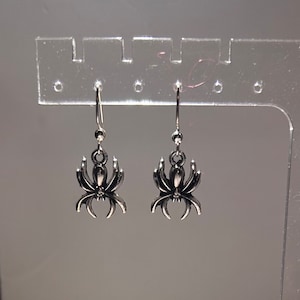 May include: A pair of silver spider earrings hanging from a display stand.