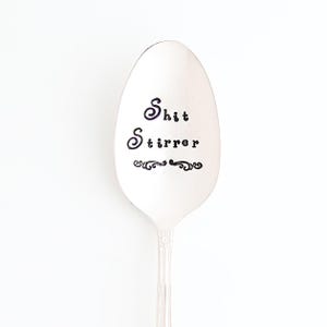 May include: A silver spoon with the words "Shit Stirrer" engraved on the front.
