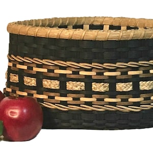 May include: A black woven basket with a brown and tan patterned rim and a braided rope design. The basket is filled with red apples.