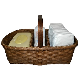 May include: A brown wicker basket with a wooden handle, divided into three sections. The basket contains a package of baby wipes, a bottle of baby lotion, and a stack of diapers.