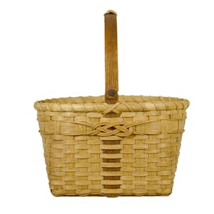 May include: A woven basket with a wooden handle. The basket is made of natural materials and has a light brown color. The handle is made of dark brown wood and has a knot at the top.