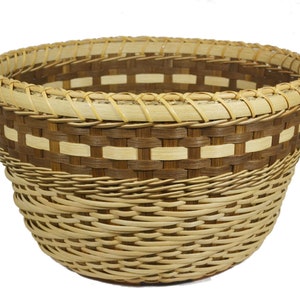 May include: A woven basket with a brown and natural colored pattern. The basket is round and has a wide opening.