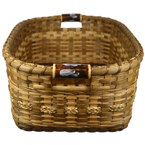 May include: A woven basket with two brown handles with white accents. The basket is made of natural materials and has a rectangular shape.