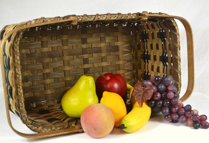 May include: A woven basket filled with fruit, including a red apple, a yellow pear, a yellow peach, a yellow lemon, a yellow banana, and a bunch of purple grapes.