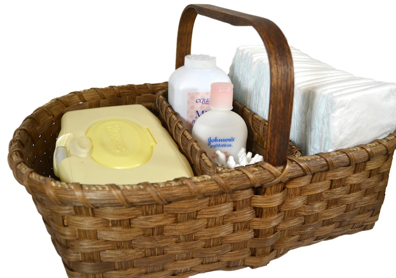 May include: A brown wicker basket with a wooden handle, divided into three sections. The basket contains baby wipes, baby lotion, baby powder, and diapers.