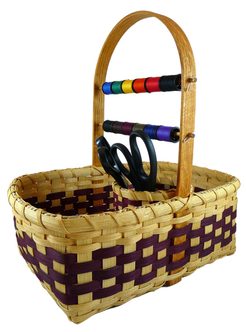 May include: A woven basket with a wooden handle and two compartments. The basket has a purple and natural woven pattern. The handle has two wooden dowels with spools of thread on them. There are also two pairs of scissors in the basket.
