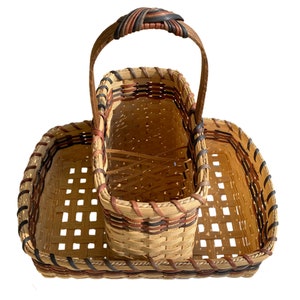 May include: A woven wicker basket with a handle and three compartments. The basket is made of natural brown wicker with black and red accents.
