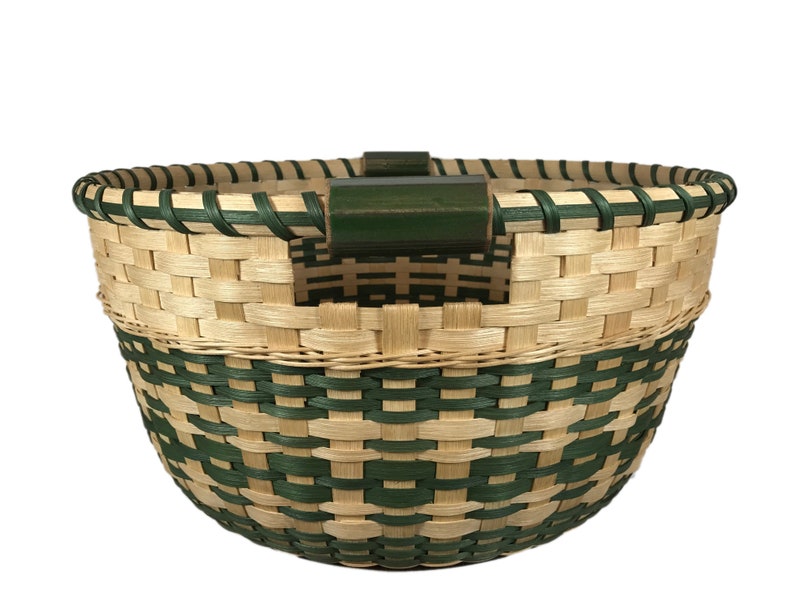 May include: A woven basket with a green and natural colored pattern. The basket has a green wooden handle.