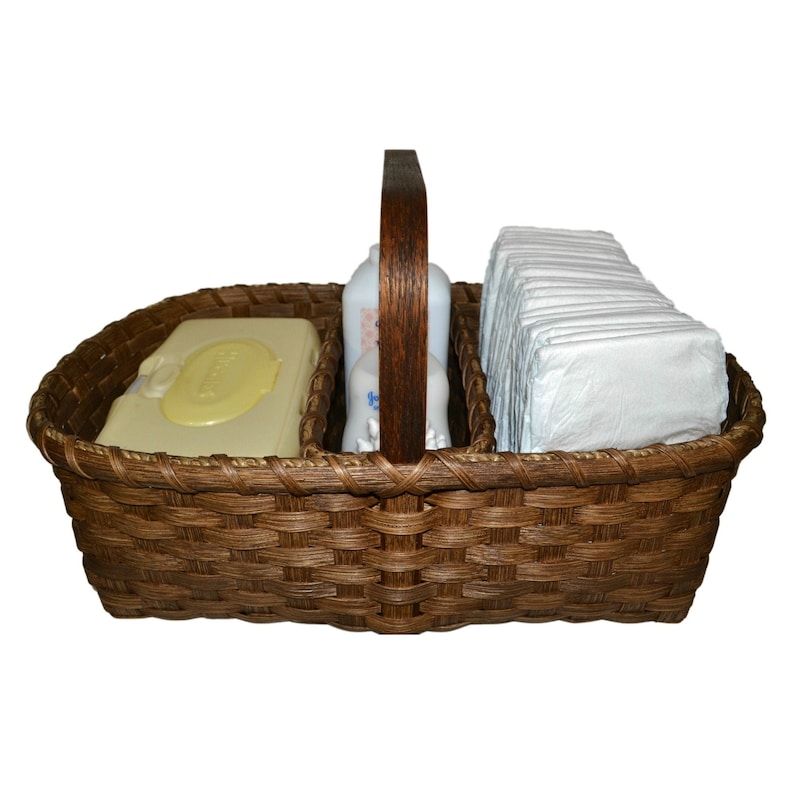May include: A brown wicker basket with a wooden handle, divided into three sections. The basket contains a package of baby wipes, a bottle of baby lotion, and a stack of diapers.