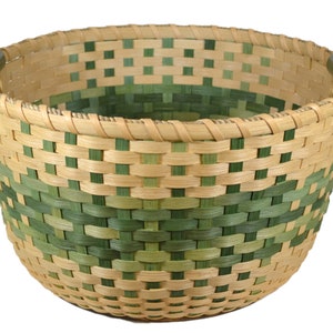 May include: A woven basket with green and natural colored reeds. The basket has two wooden handles.