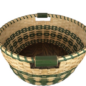 May include: A woven basket with a green and natural colored pattern. The basket has two green handles and a wooden base.