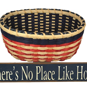 May include: A woven basket with red, white, and blue stripes, sitting on a wooden sign that reads "There's No Place Like Home".
