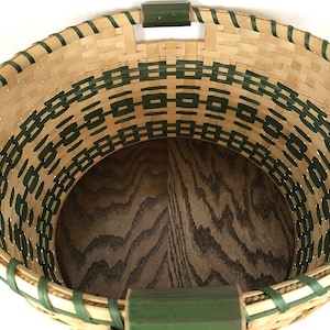 May include: A woven basket with a green and natural colored pattern. The basket has a wooden base and two green handles.