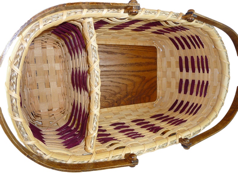 May include: A woven basket with a burgundy and natural colored pattern. The basket has a wooden base and a wooden handle.