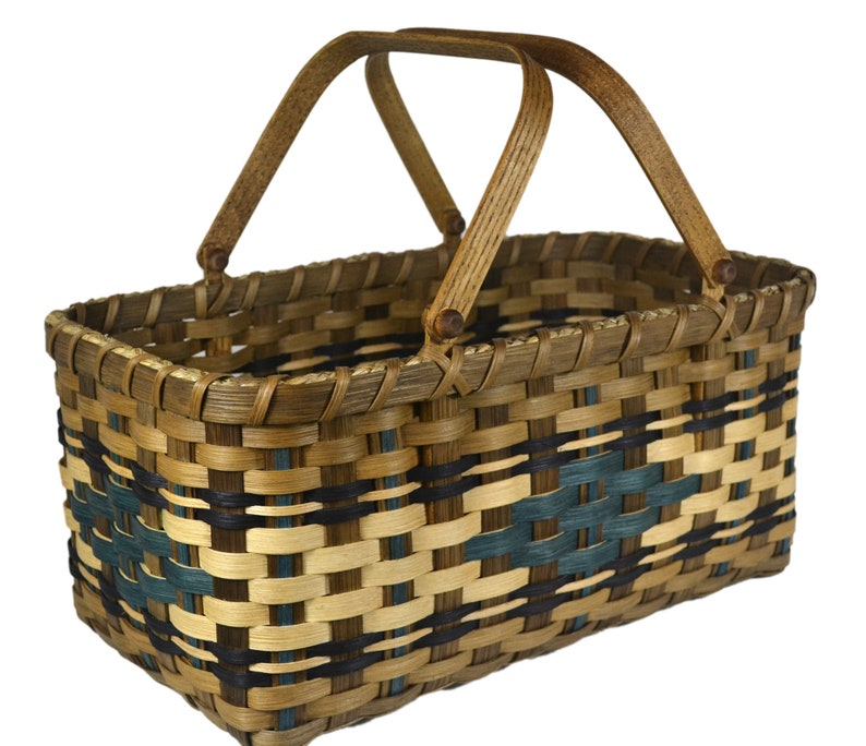 May include: A woven basket with a brown wooden handle. The basket is made with natural brown, black, and teal colored woven reeds.