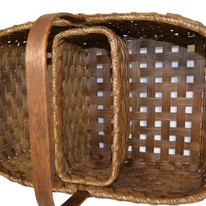 May include: A set of two brown woven baskets with a wooden handle. The larger basket has a smaller basket inside of it.