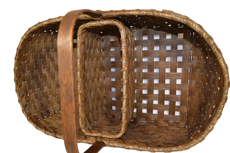 May include: A set of two brown woven baskets with a wooden handle. The larger basket has a smaller basket inside of it.