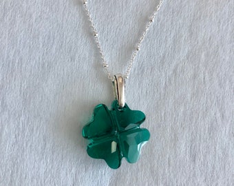 Puede incluir: Un collar de cadena de plata con un colgante de trébol de cuatro hojas verde.