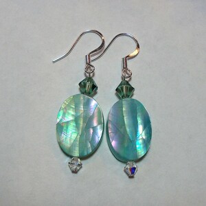 Puede incluir: Un par de pendientes de plata con cuentas ovaladas de color turquesa iridiscente y detalles de cristal verde.