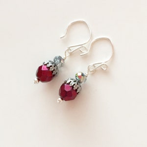 May include: A pair of silver dangle earrings with a red faceted glass bead and a silver filigree charm on each earring.
