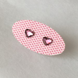 May include: A pair of pink heart-shaped stud earrings on a pink polka dot card.