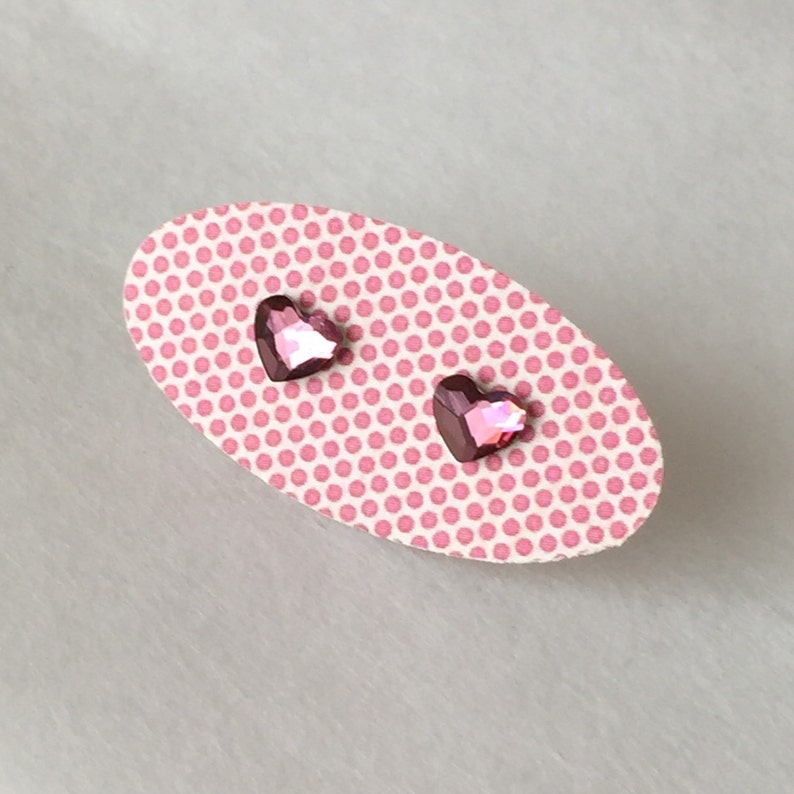 May include: A pair of pink heart-shaped stud earrings on a pink polka dot card.