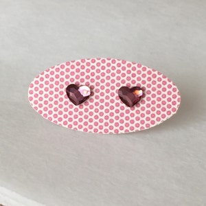 May include: A pair of heart-shaped earrings with pink iridescent stones on a pink polka dot background.