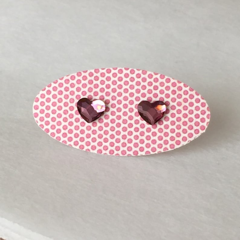 May include: A pair of heart-shaped earrings with pink iridescent stones on a pink polka dot background.