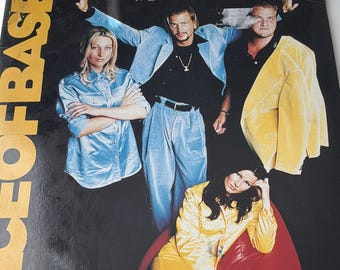 May include: Vinyl record cover for Ace of Base featuring the song Beautiful Life. The artwork displays four individuals in colourful attire, including a light blue shirt, a light blue suit, a yellow jacket, and a yellow top, against a black background.