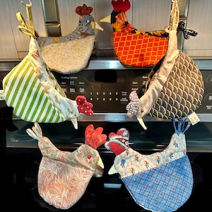 May include: Six fabric chicken-shaped oven mitts in various patterns and colors, including green stripes, floral prints, orange geometric shapes, and blue plaid. Each mitt features a red comb and a hanging loop, displayed in a group.