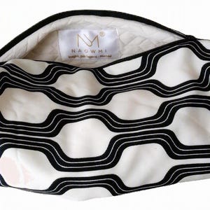 May include: A zippered pouch featuring a white and black wavy geometric pattern. The interior is lined with a quilted white fabric and includes a white label with the text NAOWMI and a logo. The pouch has a black zipper closure along the top.