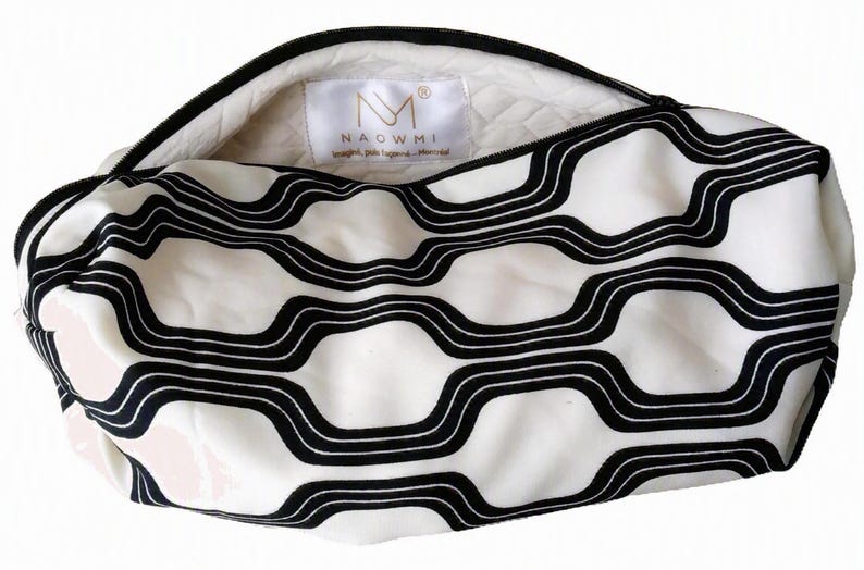 May include: A zippered pouch featuring a white and black wavy geometric pattern. The interior is lined with a quilted white fabric and includes a white label with the text NAOWMI and a logo. The pouch has a black zipper closure along the top.