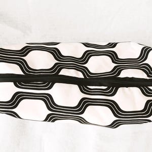 May include: A rectangular zippered pouch featuring a repeating black and white wavy geometric pattern. The fabric case has a black zipper closure running along the top center, with a soft, structured shape and a consistent graphic design.