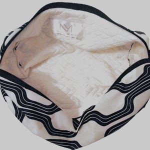 May include: A white and black zippered pouch with a wavy line pattern on the exterior. The interior is lined with a white quilted fabric featuring a rectangular brand label with the text NM and the word NAOWMI printed below it.